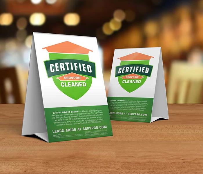 Table tent signs describing the Certified: SERVPRO Cleaned program on top of a wooden table.